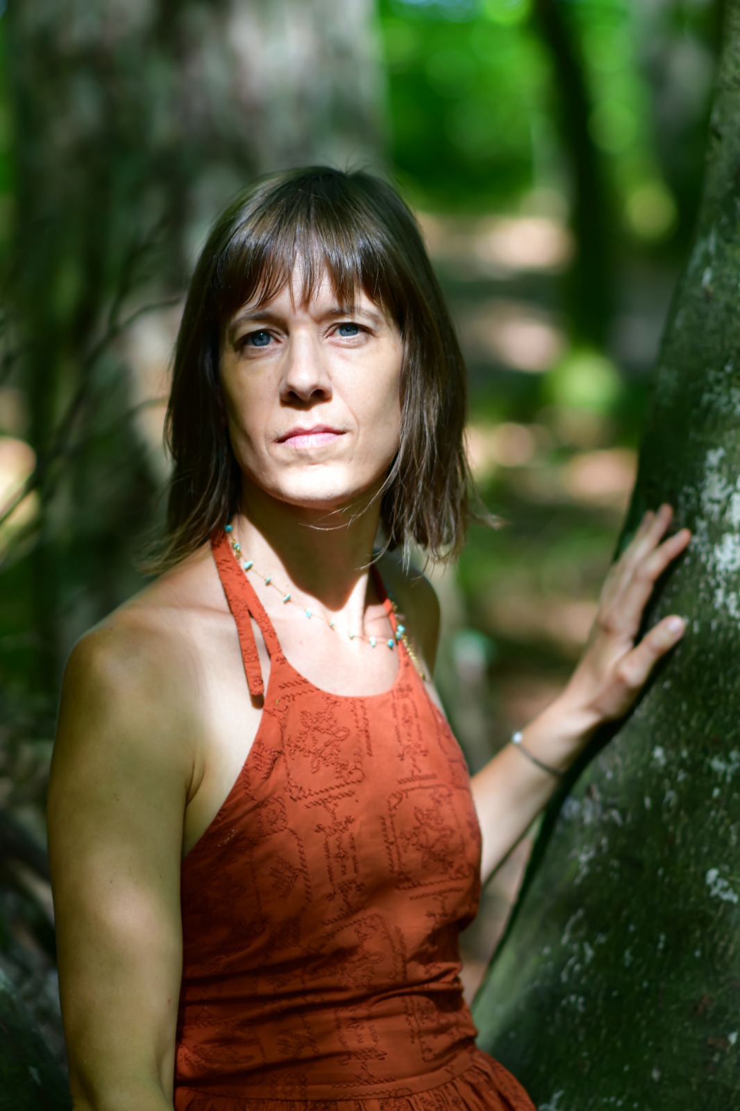 Clara André posant dans un bois, la main touchant l'écorce d'un arbre