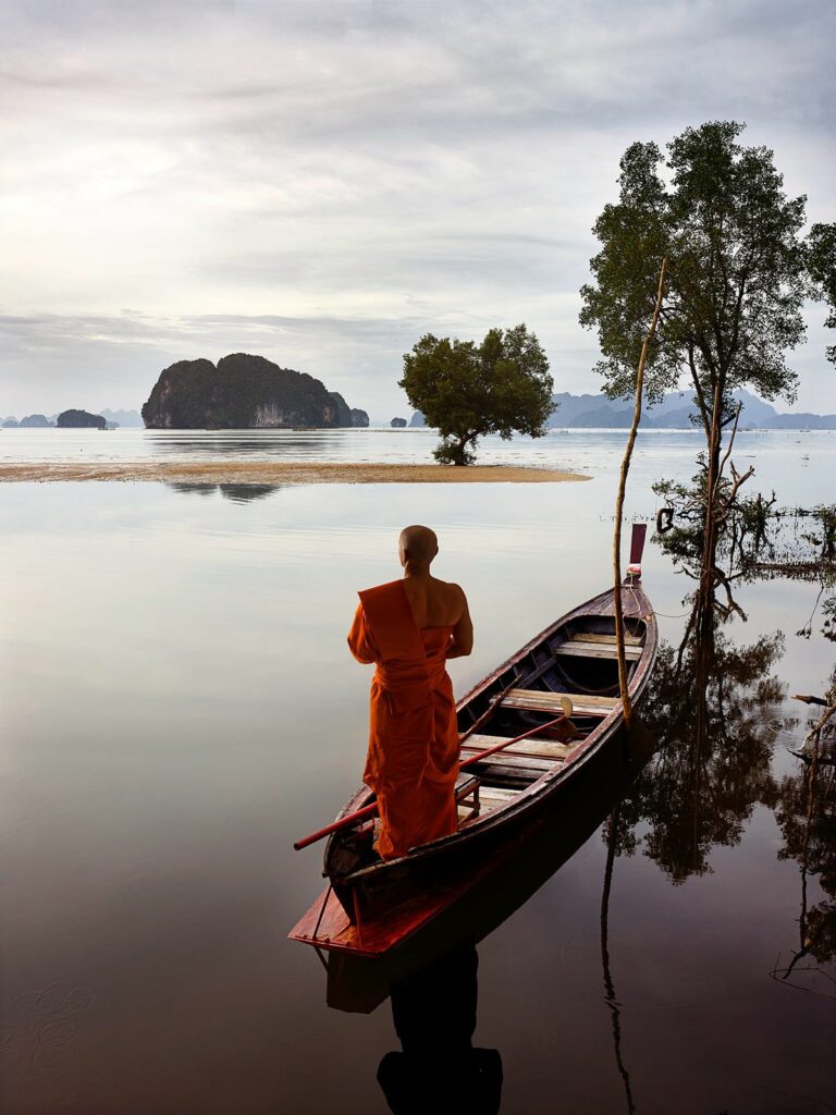 Photo zen méditative et contemplative montrant un moine debout sur une barque, présent à la beauté du matin calme sur un lac sans agitation.