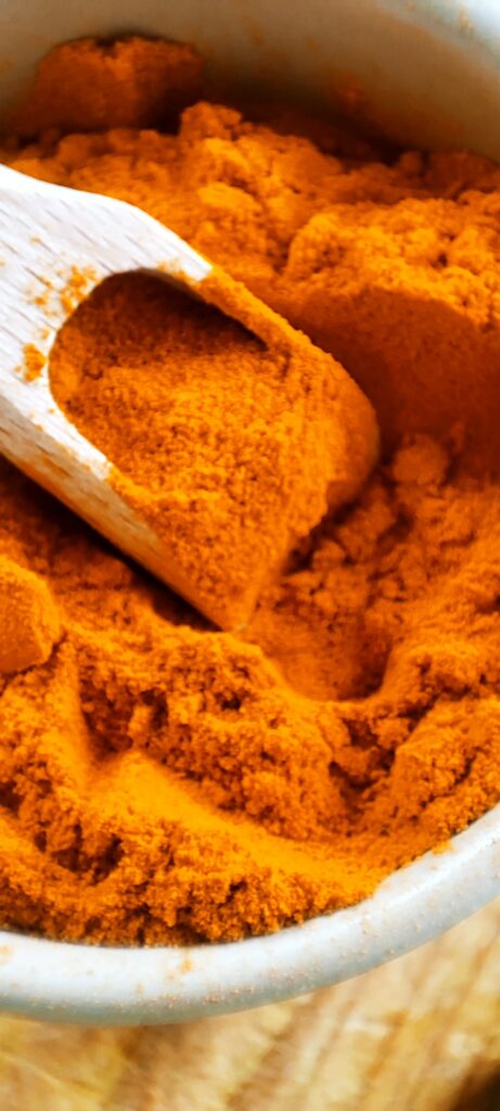 Curcuma moulu du Sri Lanka dans pot en terre et cuillet en bois, couleur intense or et safran