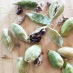 Gousses de cardamome verte ouverte et graines noires sur planche en bois