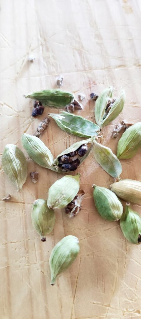 Gousses de cardamome verte ouverte et graines noires sur planche en bois